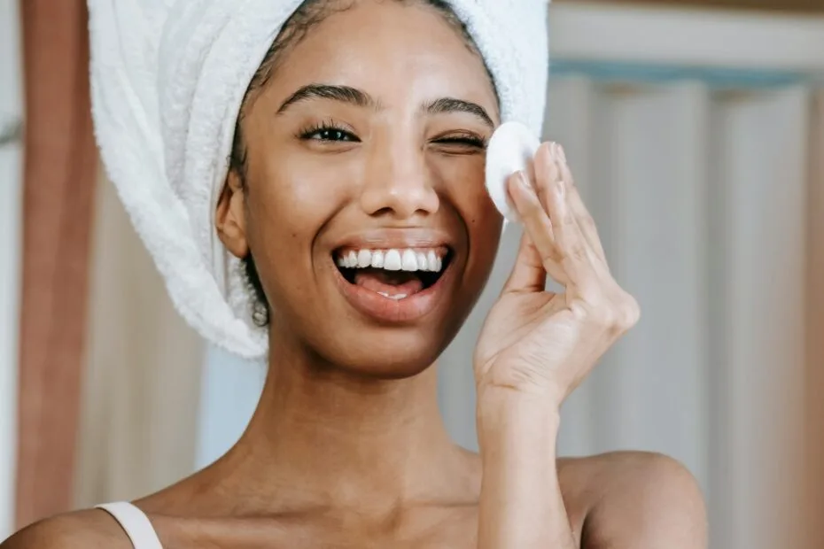 mulher negra sorrindo, com uma toalha branca na cabeça fazendo skincare de noite